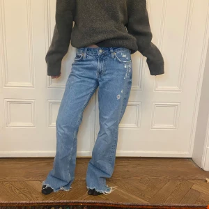 Blå jeans med slitna detaljer - Snygga blå jeans med slitna detaljer och en avslappnad passform. De har en klassisk femficksdesign och är perfekta för en casual look. Jeansen har en hög midja och raka ben som ger en tidlös stil. Säljer för att dem är för långa på mig…