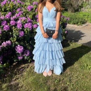 Ljusblå långklänning med volanger - Jag säljer min super fina ljusblåa balklänning som jag andvände förra året. Super fin från bubbelroom i storlek 38, den är lite smutsig längst ner men inget som man lägger märket till inga defekter skriv gärna vid frågor!❤️