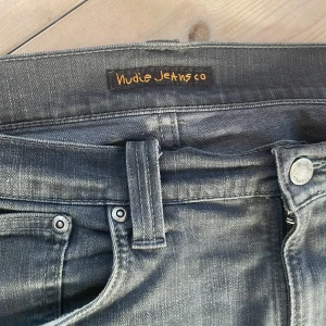 Grå jeans från Nudie Jeans - Snygga grå jeans från Nudie Jeans med en klassisk femficksdesign. De har en dragkedja och knapp framtill samt bälteshällor. Perfekta för en stilren look. Bra skick