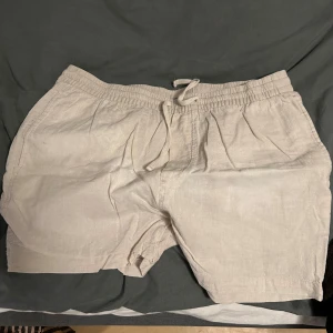 Beige linne shorts från H&M - Säljer ett par bekväma beige shorts från H&M. De har en elastisk midja med snörning för justerbar passform. Perfekta för varma dagar med sin lätta och luftiga design.