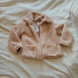 Beige teddyjacka - Mysig beige teddyjacka med långa ärmar och två fickor framtill. Perfekt för kyliga dagar när du vill hålla dig varm och stilren. Jackan har en klassisk krage och är i en mjuk och fluffig teddytextur.