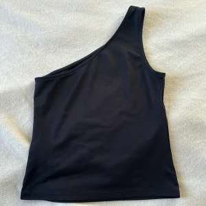 Svart oneshoulder topp - Snygg svart oneshoulder topp i ett stilrent och enkelt utförande. Perfekt för en trendig look.