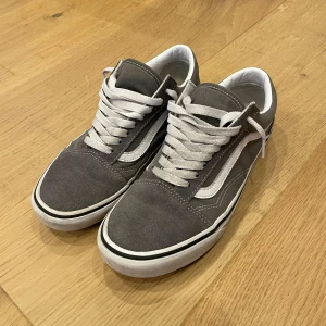 Vans Sneakers Old Skool  - Säljer nu mina snygga grå sneakers i storlek 40 från Vans därför att de blivit för små. Skorna har Vans ikoniska vita sidostrimma och är perfekta för en avslappnad stil. De är tillverkade i ett slitstarkt material som ger en skön passform. Mockan och hela skon är i nyskick - endast använda varsamt under en kort period. Bara att höra av sig vid funderingar eller extra bilder!