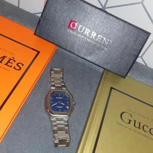  Navy Blue Klocka  - Snygg silverfärgad klocka med blå urtavla och. Den har en rektangulär boett och länkarmband i metall. Helt ny. Skick 10/10. Följer med länkbitar så man kan ändra storleken