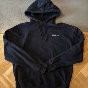 Svart hoodie från Axel Arigato - Säljer en svart hoodie från Axel Arigato med tryck både fram och bak. Den har en klassisk design med huva och dragsko samt långa ärmar. Perfekt för en avslappnad stil.
