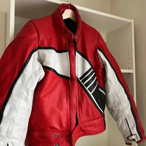 Vintage Röd skinnjacka/skinnställ - Säljer en vintage röd skinnjacka med vita och svarta detaljer. Jackan har ett motoscykel skinnställ där den går att ta isär till 2 olika plagg. Har själv använt endast jackan. Finns lite märken och missfärgningar, men överlag gott skick frpn att vara från 50-talet. Perfekt för dig som vill sticka ut med en unik stil.