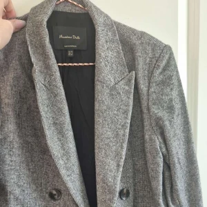 Grå rutig kavaj från Massimo Dutti - Snygg grå rutig kavaj från Massimo Dutti med dubbelknäppning och klassisk krage. Perfekt för en stilren look. Kavajen har långa ärmar och en elegant passform.