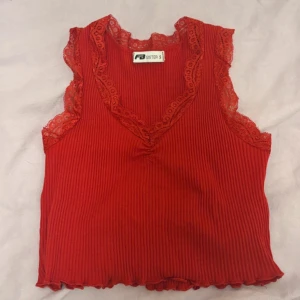 Röd ribbad topp med spetsdetaljer - Snygg röd ribbad topp från Sister S med spetsdetaljer vid ärmar och hals. Toppen är ärmlös och har en v-ringad design som ger en feminin touch. 