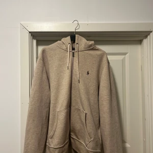 Grå Zip hoodie från Ralph Lauren Medium - Säljer en stilren grå hoodie från Ralph Lauren med dragkedja och den klassiska loggan på bröstet. Tröjan har en justerbar huva och praktiska fickor framtill. Perfekt för en avslappnad look.