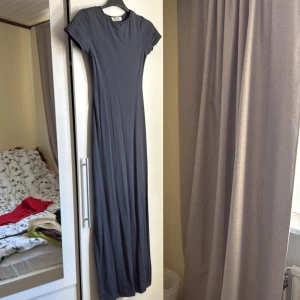 Mörkgrå långklänning - Säljer en elegant mörkgrå/ blå långklänning. Klänningen har en enkel och stilren design med korta ärmar och rund hals. Perfekt för en minimalistisk look. 