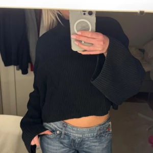 stickad polotröja - Säljer en svart stickad polotröja med croppad design. Tröjan har långa ärmar och en hög krage som ger en stilren look. Perfekt för kyligare dagar och lätt att matcha med olika outfits.