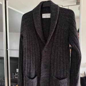 Mörkgrå cardigan från These Glory Days - Säljer en stilren mörkgrå kofta från These Glory Days. Koftan har en ribbad design med långa ärmar och två fickor framtill. Stl M