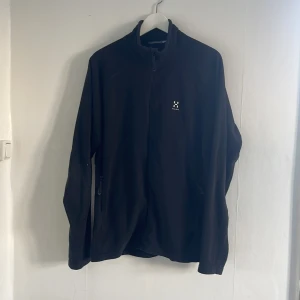 Svart fleecejacka från Haglöfs - Säljer en svart fleecejacka från Haglöfs i storlek XL. Jackan har en dragkedja framtill och är långärmad. Perfekt för kyligare dagar och outdoor-äventyr. Haglöfs-logga på bröstet ger en stilren touch.