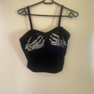 Svart tubtopp med strassdetaljer - Snygg svart tubtopp med tunna axelband och coola strassdetaljer framtill som ger en edgy look. Perfekt för en utekväll eller fest. Toppen är figurnära och ger en stilren siluett.