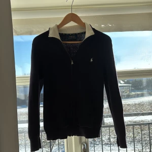 Svart tröja med dragkedja från Polo Ralph Lauren - Säljer en stilren marinblå tröja med dragkedja från Polo Ralph Lauren. Tröjan har en vit krage och det klassiska logotypbroderiet på bröstet. Perfekt för en avslappnad men ändå snygg look. Nypris 2599kr mitt pris 599kr. Perfekt nu till hösten. 