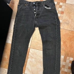 Svarta jeans från Levi's 501 - Säljer ett par klassiska svarta Levi's jeans med knappgylf. De har en rak passform och är tillverkade i slitstarkt denim. Perfekta för en stilren look.