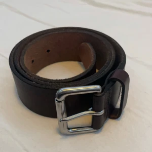 Ralph Lauren Bälte - Snyggt brunt skärp i skinn från Polo Ralph Lauren med en stilren silverfärgad spänne. Perfekt för att ge en klassisk touch till din outfit. Skärpet har en enkel design med präglad logotyp.