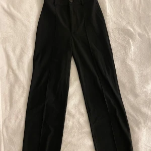 Svarta kostymbyxor - Eleganta svarta kostymbyxor från Pull&Bear med hög midja och knäppning fram. Byxorna har en rak form och är väldigt bekväma.