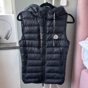  Moncler väst - Säljer en snygg svart dunväst från Moncler med dragkedja och huva. Västen har ett stilrent quiltat mönster och Moncler-logga på bröstet. Perfekt för kyliga dagar när du vill hålla stilen.Köpt i moncler butiken i Stockholm limited edition exemplar endast 2 par i hela Sverige såldes storlek 0 den minsta så den passar xs-s den har luva och snören som inte de vanliga västarna har , nypris 17 000 så är osäker om jag vill släppa om ja släpper ska de va bra pris