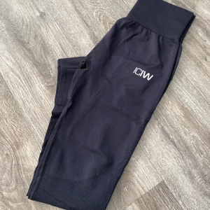 Svarta tights från ICANIWILL - Snygga svarta tights från ICANIWILL med hög midja och ribbad detalj vid midjan. Perfekta för träning med en tight passform och stilren design. Logotypen är diskret placerad på benet.
