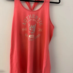 Rosa linnetopp från Puma - Snygg rosa linnetopp från Puma med tryck framtill. Toppen har en sportig design med brottarrygg och är perfekt för träning eller en avslappnad dag. Tillverkad i ett mjukt och bekvämt material.