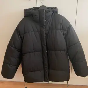 Säljer en svart pufferjacka från Monki med huva och dragkedja. Jackan har en oversized passform och är perfekt för kalla dagar. Den är stilren och enkel att matcha med olika outfits.