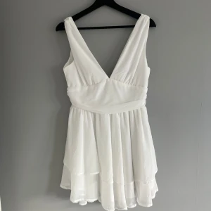 Vit ärmlös klänning med v-ringning - Säljer en elegant vit klänning med v-ringning och ärmlös design. Klänningen har en luftig och flödande kjol som ger en romantisk känsla. Perfekt för sommarens alla tillfällen och även studenten!