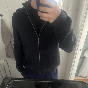 Svart stickad tröja från These Glory Days - Säljer en stilren svart stickad tröja från These Glory Days. Tröjan har en dragkedja framtill och långa ärmar, perfekt för kyligare dagar. Den är både bekväm och snygg, ett måste i garderoben!