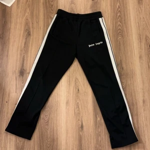 Svarta byxor från Palm Angels - Snygga svarta byxor från Palm Angels med vita sidoremsor och logga på låret. Med ett väldigt bra skick!!