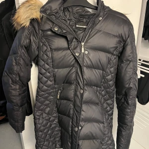 Svart dunjacka från Rockandblue - Snygg och varm dunjacka från Rockandblue med pälskantad huva (som också är avtagbar) Jackan har dragkedja och knappar framtill samt en cool patch på ärmen. Perfekt för kalla dagar! Mycket fint skick. Står 38 men den är rätt tajt🙂