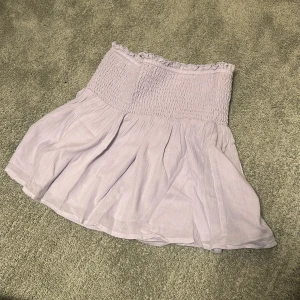 Ljuslila tubtopp från Gina Tricot - Säljer en söt ljuslila tubtopp från Gina Tricot. Toppen har en smockad överdel och ett flödande tyg nedtill som ger en luftig känsla. Perfekt för varma dagar eller som ett lager under en jacka. Tröjan har även bortagbara axelband