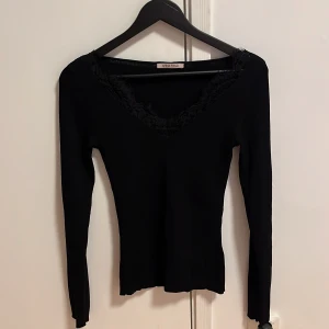 Svart långärmad topp från Anna Field - Snygg svart topp från Anna Field med spetsdetaljer runt v-ringningen. Den är långärmad och har en elegant design som passar perfekt för olika tillfällen. Perfekt för dig som vill ha en stilren look.