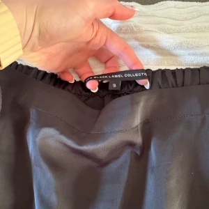 Svart kjol från lager 157 - Elegant svart kjol från Black Label Collection i storlek S. Kjolen har en enkel och stilren design med elastisk midja för bekväm passform. Perfekt för en chic och sofistikerad look.