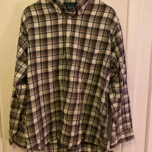 Rutig skjorta från Sebago - Säljer en stilren rutig skjorta från Sebago i jordnära färger som beige, grön och blå. Skjortan har långa ärmar och knappar framtill. Perfekt för en avslappnad look.