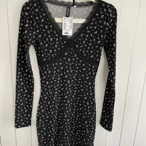 Svart blommig klänning från H&M  - Snygg svart klänning med små blommor och ribbad struktur från H&M. Den har en v-ringad spetskant.