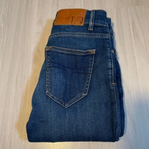 Skinny jeans från Tiger of Sweden - Snygga blå jeans från Tiger of Sweden med klassisk femficksdesign och orange sömmar. De har en smal passform och är tillverkade i ett slitstarkt denimtyg. Perfekta för en stilren look.