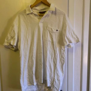 Vit pikétröja från Morris - Säljer en klassisk vit pikétröja från Morris i storlek XL. Tröjan har korta ärmar och en liten bröstficka med en diskret logga. Perfekt för en stilren och avslappnad look.