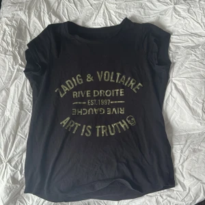 Svart t-shirt från Zadig & Voltaire - Snygg svart t-shirt från Zadig & Voltaire med guldigt  tryck. Korta ärmar.  Storlek S! Några små hål längt ner på tröjan på framsidan som går att sy igen. Nypris är ca 800kr!🩷