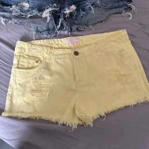 Gula jeansshorts med slitningar - Snygga gula jeansshorts med slitna detaljer och fransig kant. Perfekta för en avslappnad sommarlook. De har en knapp och dragkedja framtill samt klassiska fem fickor.
