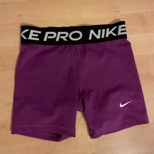 Lila träningsshorts från Nike - Snygga lila träningsshorts från Nike med svart resårmidja och vit logga. Stl L i barn men skulle säga att det motsvarar typ en XS i vuxenstorlek. Väldigt fina, använda fåtal gånger, nästan inga tecken på användning💕
