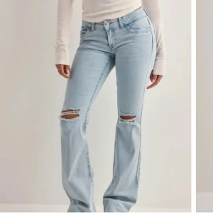 Ljusblå bootcut jeans med slitningar låg midja - Snygga ljusblå jeans i bootcut-stil med slitningar på knäna storlek 34. De har en låg midja och broderade detaljer på bakfickorna. Perfekta för en avslappnad look. Skriv om fler bilder prislappen är på aldrig använda ny skick 