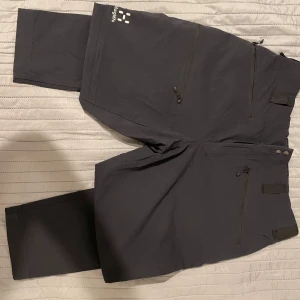 Svarta byxor från Haglöfs - Säljer ett par svarta byxor från Haglöfs i storlek 44. Byxorna har flera praktiska dragkedjor och är perfekta för utomhusaktiviteter. De är designade för kvinnor och har en bekväm passform.