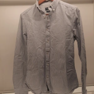 Randig skjorta från East West - Säljer en stilren randig skjorta från East West i storlek S. Skjortan har en klassisk krage och knappar framtill. Perfekt för en avslappnad men ändå uppklädd look.