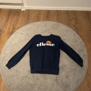 Mörkblå sweatshirt från Ellesse - Säljer en snygg mörkblå sweatshirt från Ellesse med deras ikoniska logga tryckt på framsidan. Tröjan har långa ärmar och en klassisk rund halsringning. Perfekt för en avslappnad stil.