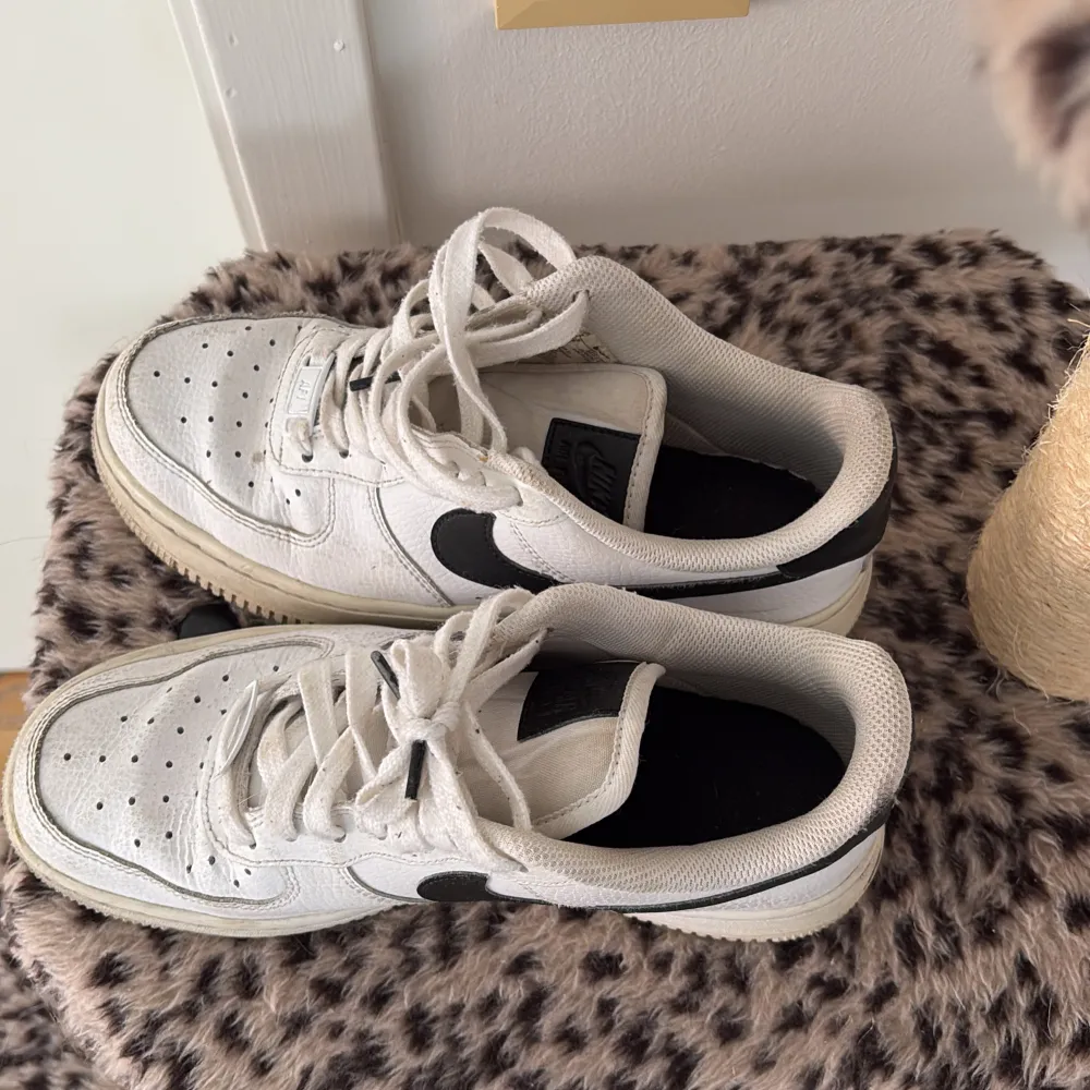 Säljer ett par klassiska Nike Air Force sneakers i vitt med svarta detaljer. Skorna har snörning och en robust sula. Perfekta för en stilren look.. Kengät.