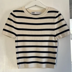 Randig kortärmad tröja från Zara - Säljer en stilren randig tröja från Zara i svart och beige. Tröjan har korta ärmar och en rund halsringning, perfekt för en avslappnad look. Passar bra till både jeans och kjol. 🖤🤍