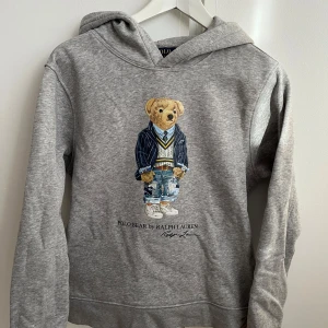 Grå hoodie från Ralph Lauren med björnmotiv - Säljer en grå hoodie från Ralph Lauren med ett björnmotiv på framsidan. Tröjan har en klassisk huva.