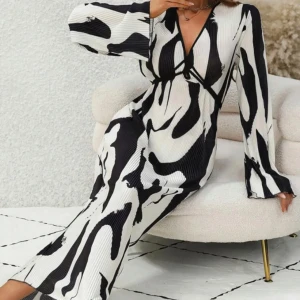 Svartvit långklänning med abstrakt mönster - Snygg svartvit långklänning med abstrakt mönster och v-ringning. Klänningen har långa ärmar och en elegant passform som ger en stilren look. Perfekt för en chic och modern stil.