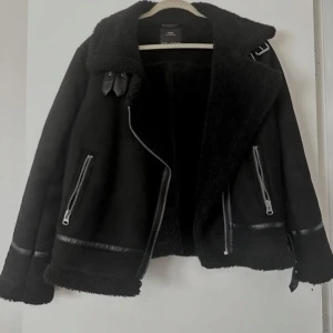 Svart jacka med fuskpäls - Snygg svart jacka från Zara med fuskpälsfoder och dragkedja. Jackan har långa ärmar och två framfickor med dragkedjor. Perfekt för kyligare dagar med sin stilrena design och bekväma passform.