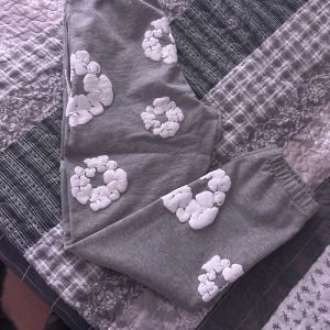 Grå mjukisbyxor med vita blommor - Säljer ett par grå mjukisbyxor med vita blommönster. Byxorna har en bekväm passform med elastisk midja och snörning. Perfekta för en avslappnad stil.